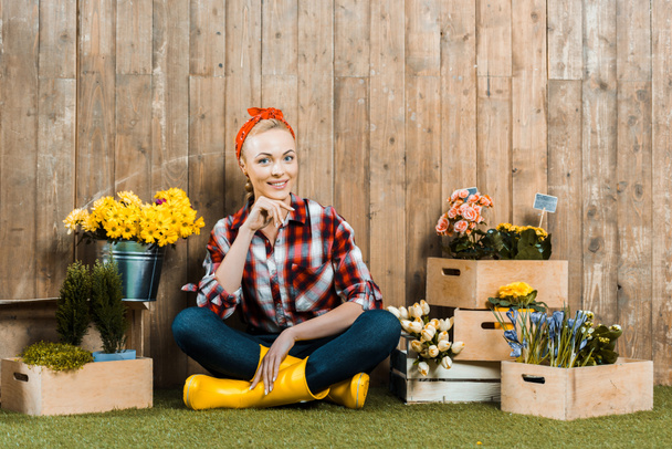 beautiful woman sitting with crossed legs near flowers in wooden boxes - Foto, imagen