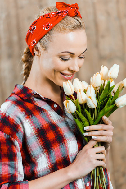 cheerful woman smiling while smelling tulips  - Fotó, kép