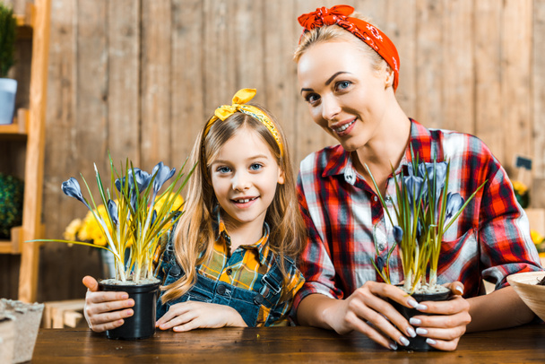 happy mother and adorable daughter looking at camera while holding pots with flowers - Foto, Bild
