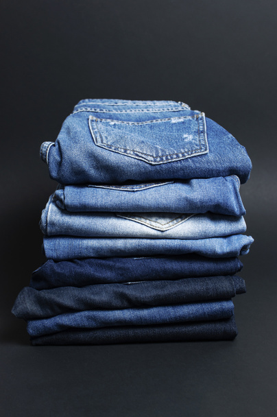 Stack of various blue jeans on black background. Beauty and fashion, clothing concept. Detail of nice blue jeans. Jeans texture or denim background. Collection of jeans - Photo, Image