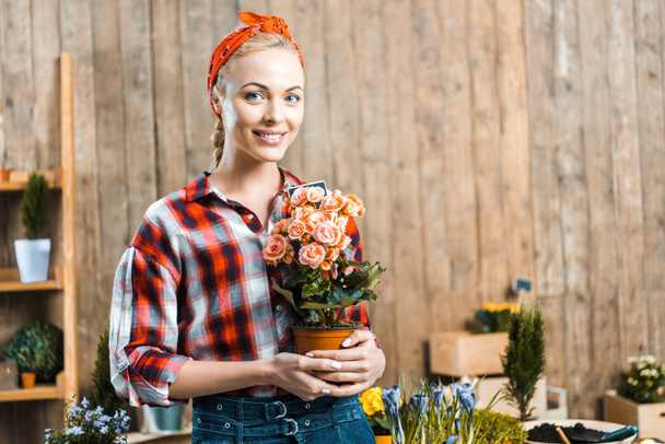 cheerful woman standing and holding pot with flowers - Фото, зображення