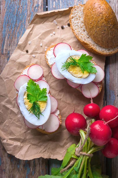 Fresh toast sandwiches with egg, radish, cucumber and soft cheese, decorated with parsley on craft paper on a rustic wooden background. - Photo, Image