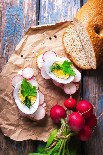 Τοστ φρέσκα σάντουιτς με αυγό, ραπανάκια, αγγούρι και μαλακό τυρί, διακοσμημένο με μαϊντανό σε χαρτί βιοτεχνίας σε ρουστίκ ξύλινα φόντο. - Φωτογραφία, εικόνα