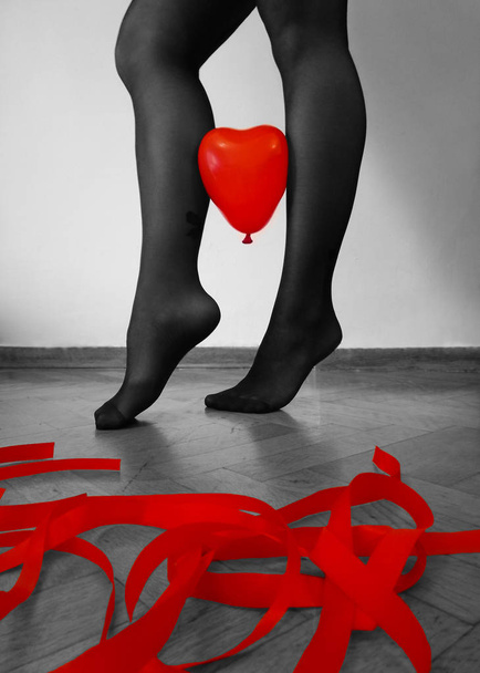 benen in zwarte panty's met een rood hart vorm ballon bedrijf op de houten vloer met rode linten - Foto, afbeelding