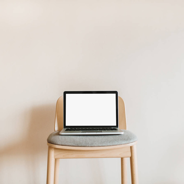 Φορητός υπολογιστής με χλεύη επάνω οθόνη ξύλινη καρέκλα σε παστέλ μπεζ φόντο. Blog, ιστοσελίδα, κοινωνικών μέσων μαζικής ενημέρωσης ήρωας κεφαλίδα πρότυπο. - Φωτογραφία, εικόνα