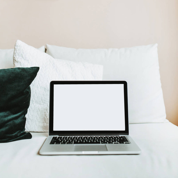 Minimal home office workspace. Laptop with mockup blank screen on bed with pillows. Blogger / freelancer business concept. - Фото, изображение
