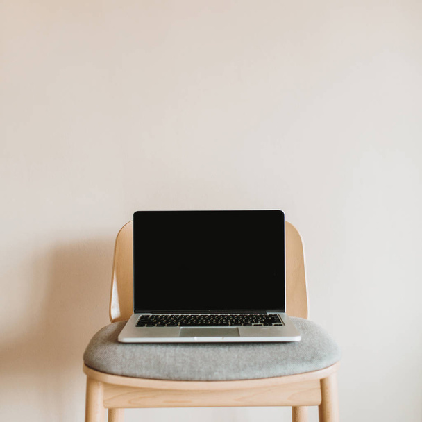 Laptop with mock up screen on wooden chair on pastel beige background. - Фото, изображение