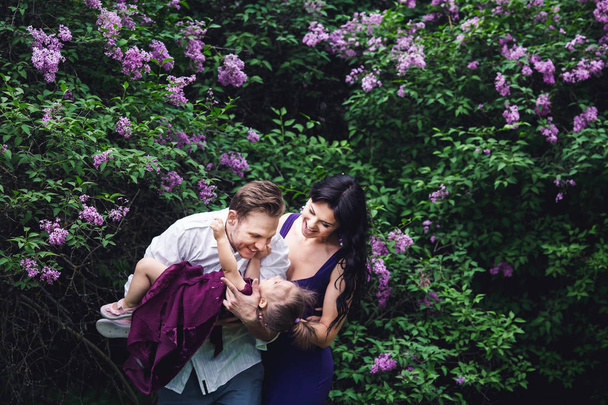 cheerful happy family hugging near lilac flowering bushes. - Foto, Imagem