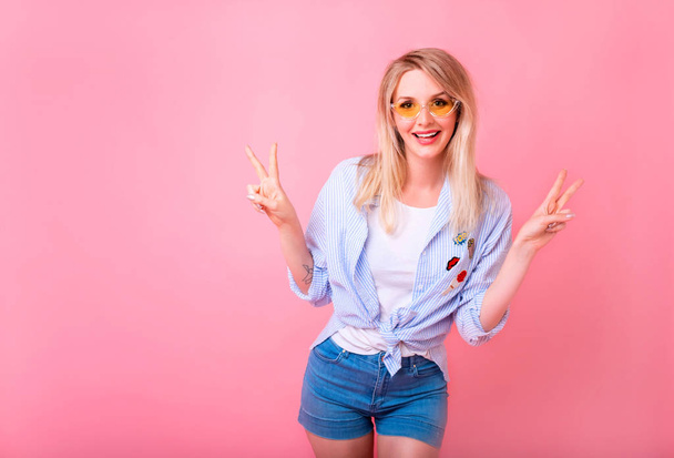 Portrait of a happy cheerful girl, young blonde woman showing peace gesture with two hands isolated over pink background - Φωτογραφία, εικόνα