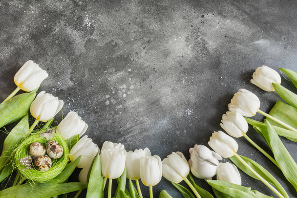 Easter pattern. Border of white tulips, colorful eggs, nest on vintage gray. Top view with copy space. - Fotoğraf, Görsel