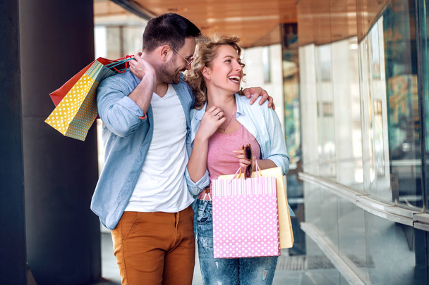 Verkauf, Konsum und Menschen-Konzept - glückliches Paar mit Einkaufstüten blickt in Schaufenster der Stadt. - Foto, Bild