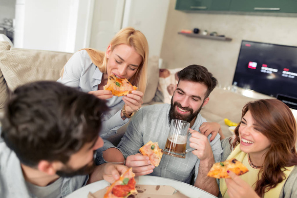 Uśmiechnięty znajomych, jedzenie pizzy i picia piwa w domu. Koncepcja wypoczynek, ludzie, jedzenie i szczęścia. - Zdjęcie, obraz