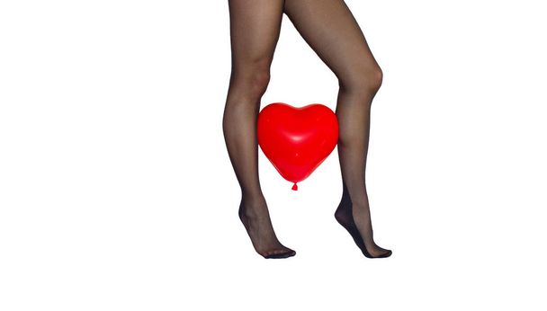 Frauenbeine auf den Zehen in schwarzen Strumpfhosen mit rotem Herzbalon zwischen auf weißem Hintergrund. - Foto, Bild