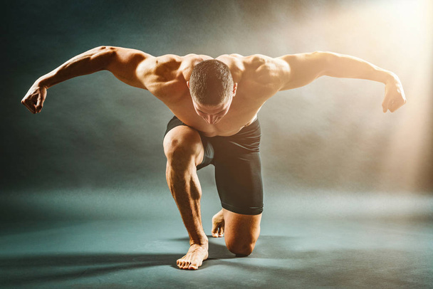 Lihaksikas mies seisoo polvella ja näyttää lihaksia
 - Valokuva, kuva