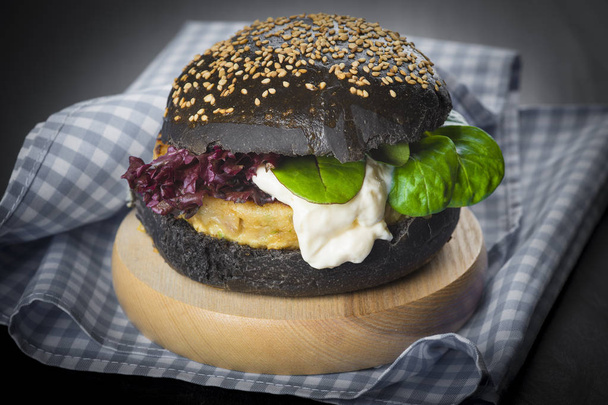 Hamburguesa de pescado en un bollo negro con semillas de sésamo y amapola y lechuga fresca y tomate
 - Foto, Imagen