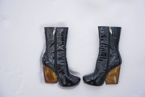pair of black female boots with high heels on white snow background. winter time season.   - Фото, изображение