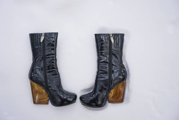 pair of black female boots with high heels on white snow background. winter time season.   - Fotó, kép