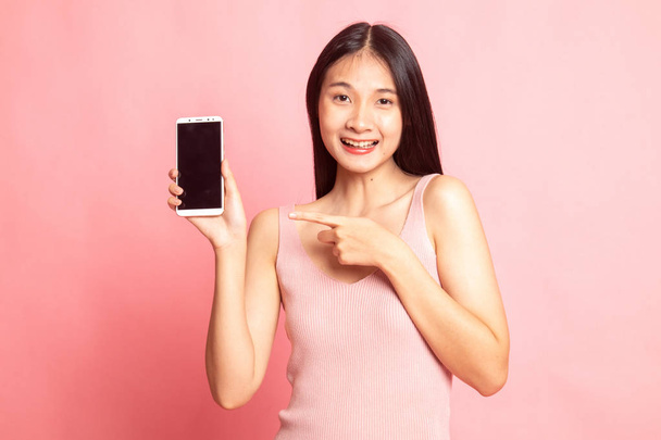 Excited Young Asian woman point to mobile phone on pink background - 写真・画像