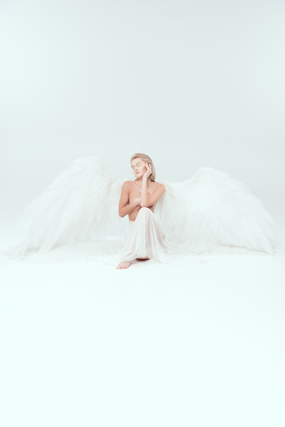 krásná žena s andělskými křídly, který zakrýval ňadra a pózování izolované na bílém s kopií prostor - Fotografie, Obrázek