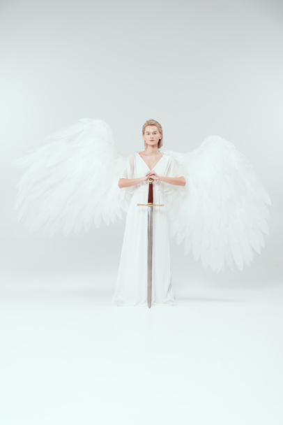 mooie vrouw met vleugels van de engel holding zwaard en poseren op witte achtergrond - Foto, afbeelding