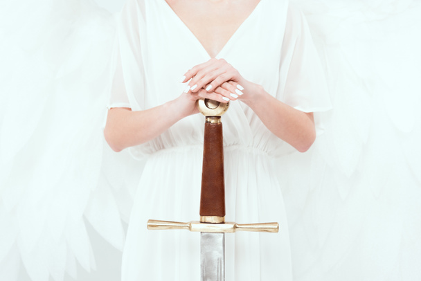 cropped view of woman with angel wings holding sword isolated on white - Foto, afbeelding
