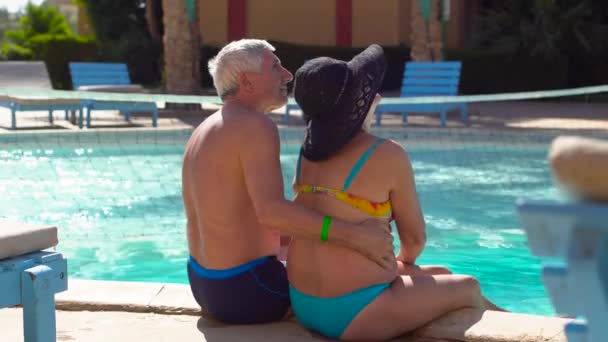 Idősebb pár pihentető, és beszél a medence a szálloda. Boldog ember élvezi a nyaralás. All inclusive. 4k - Felvétel, videó