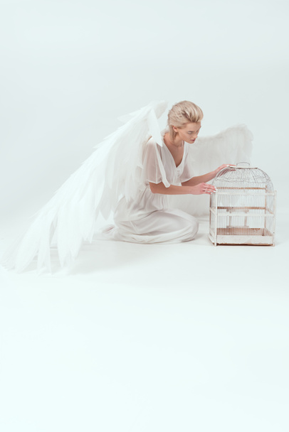 beautiful woman in angel costume with wings posing with bird cage isolated on white - Photo, Image
