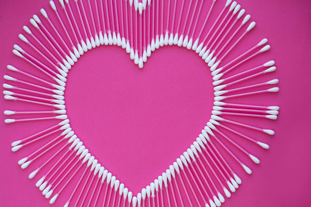 cotton buds laid out in the shape of a heart on a pink background. - Zdjęcie, obraz