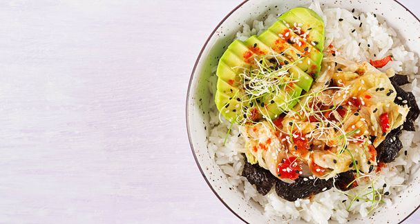 Vegan salad  with rice, pickled kimchi cabbage, avocado,  nori and sesame on bowl. Sushi-food hybrids trend. Overhead, top view, flat lay. - Photo, Image