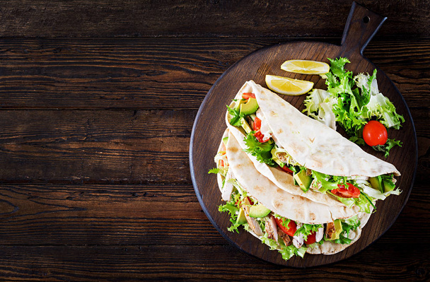 Pita bread sandwiches with grilled chicken meat, avocado, tomato, cucumber and lettuce served on  wooden background. Close up. Top view. Healthy fast food concept. - Foto, Imagem