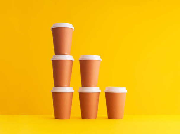 Meerdere besteedbaar koffie kopjes georganiseerd in een stapel op gele achtergrond - Foto, afbeelding