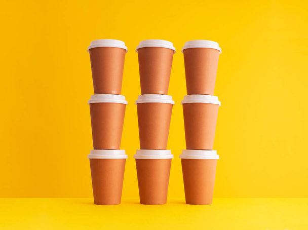 Plusieurs tasses à café jetables organisées dans une pile sur fond jaune
 - Photo, image