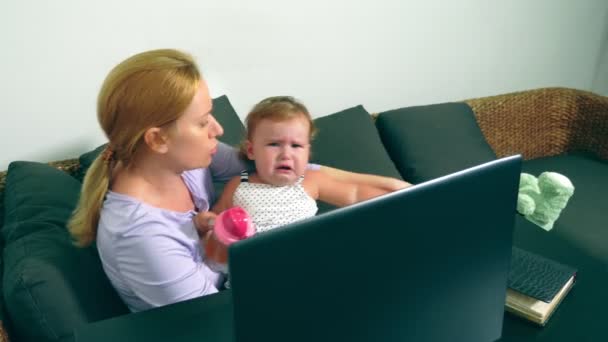 Annoyed businesswoman holding a crying baby in her arms while working on a laptop. Career mom concept, problems associated with work at home - Video