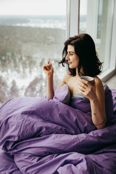 jonge brunette vrouw het drinken van thee in de ochtend zittend in de buurt van het venster  - Foto, afbeelding