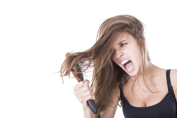 Mujer joven gritando mientras peina el pelo castaño por cepillo. Aislado sobre fondo blanco
 - Foto, Imagen