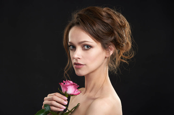 Beautiful woman with clean perfect skin holds a rose flower. Beauty model with natural nude make up. Spa and skincare. Black background - Zdjęcie, obraz