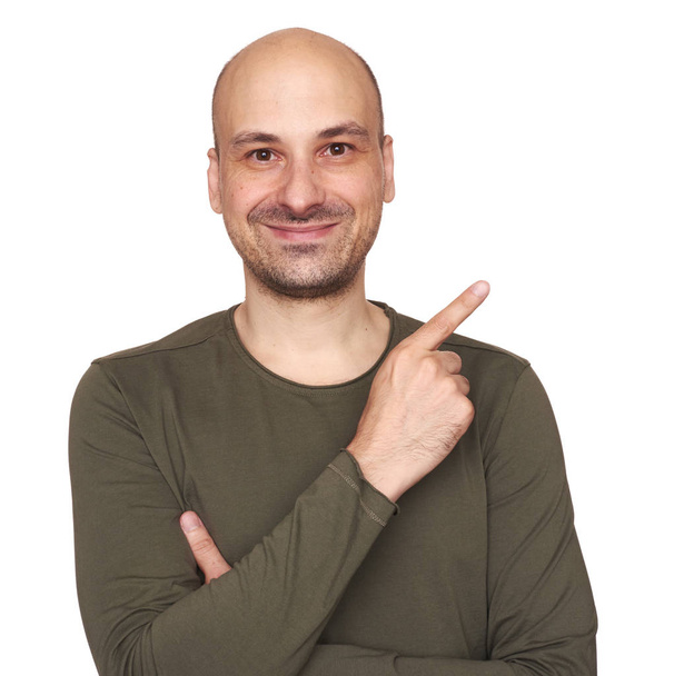 cheerful bald guy is pointing finger to copy space. Isolated on white studio background - Foto, imagen