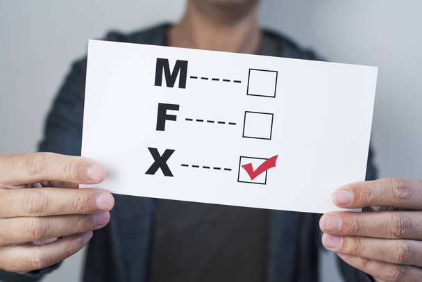 closeup of a young caucasian person holding a form with the letters M for male, F for female and X for the third gender category, written in it, with a check mark on the X - Photo, Image
