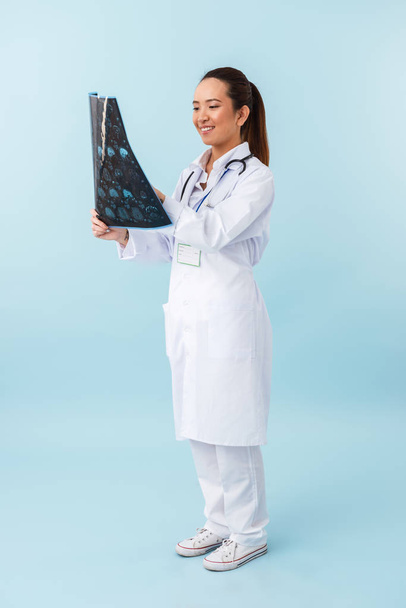Photo of a young happy woman doctor posing isolated over blue wall background with x-ray. - Photo, Image