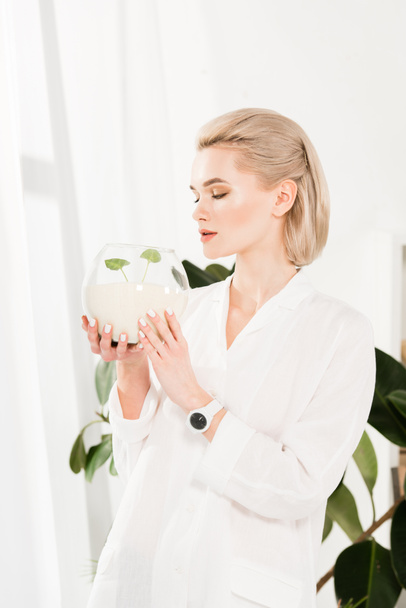 attractive woman looking at glass fish bowl with sand and green small leaves,  environmental saving concept  - Photo, image