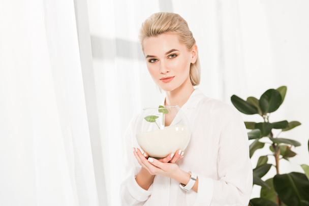 attractive woman holding glass fish bowl with sand and green leaves, environmental saving concept  - Fotoğraf, Görsel