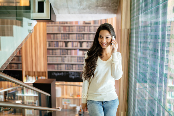 Beautiful businesswoman using phone indoors and smiling - Foto, afbeelding