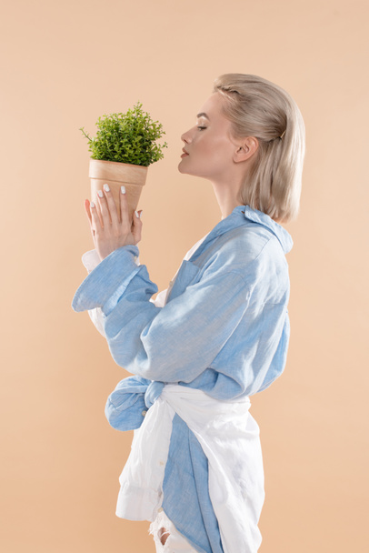 Profil kobiety trzymając garnek z roślin i stojąc w eko Odzież na białym tle na beż, środowiska zapisywanie koncepcja  - Zdjęcie, obraz