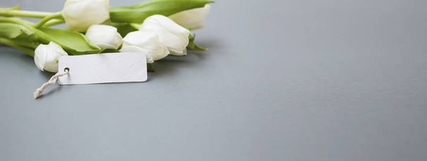 Ramo de tulipanes blancos con tarjeta de espacio de copia en blanco sobre fondo gris, vacaciones de primavera saludando naturaleza muerta
 - Foto, Imagen
