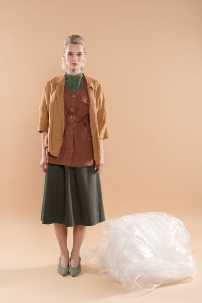 blonde girl wearing eco clothing standing near polyethylene on beige background, environmental saving concept - Photo, Image