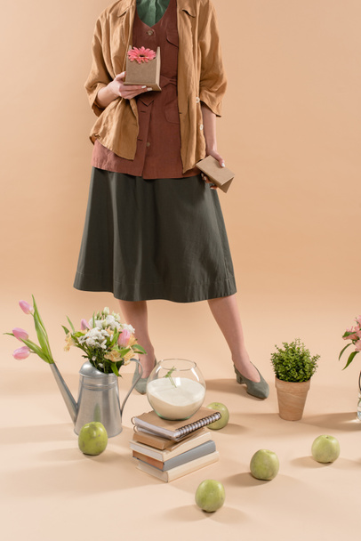 vista ritagliata di donna che tiene casa di cartone con fiore vicino a piante e fiori su sfondo beige, concetto di risparmio ambientale
 - Foto, immagini