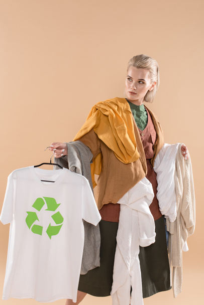 young woman holding eco clothing with recycling sign on hanger isolated on beige, environmental saving concept - Photo, Image
