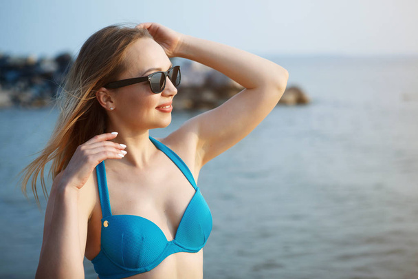 mujer en traje de baño azul y gafas de sol caminando a lo largo de la playa de arena por mar
 - Foto, imagen
