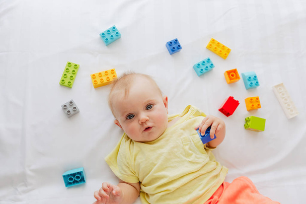 Kleine baby liggend op white linnen tussen speelgoed - Foto, afbeelding