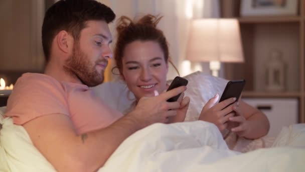 happy couple using smartphones in bed at night - Filmati, video